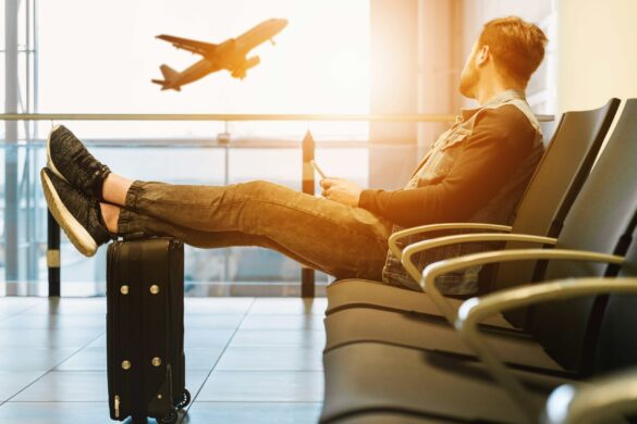 Man in airport looking at airplane, feet on carry-on. Photo by JESHOOTS.COM on Unsplash